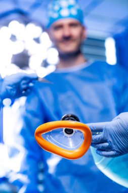 Bir tıbbi uzman anestezi maskesi tutarken, bir diğeri ameliyat sırasında hastane ameliyathanesinde ekipmanları hazırlıyor..