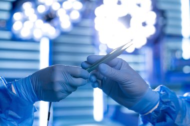 Cerrahlar steril bir odada, eldivenli ellerde cerrahi aletlerle birlikte çalışırlar. Operasyon için hazırlanan parlak ışıklar bölgeyi aydınlatıyor. Takım çalışmasına ve yeteneğe odaklan..