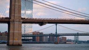 Arabalar gidiyor ve insanlar ünlü Brooklyn Köprüsü 'nün önünden geçiyor. Nehir manzarasından yapıya düşük açı görünümü.
