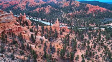 Otoyol, ABD 'nin Utah eyaletindeki Bryce Canyon Ulusal Parkı' nın kayalık arazisinden geçer. Üzerlerinde büyüyen kırmızı kaya oluşumları ve kozalaklı ağaçlar üzerine hava perspektifi..