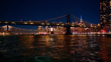 Tekneyle Manhattan Köprüsü 'nden Brooklyn Köprüsü' ne uzaklık. Arka planda New York 'un gece silueti.