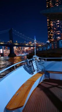 New York, ABD, 9 Aralık 2025, rıhtımda duran tekneden New York 'un gece manzarasını izlemek. Metropolis ufuk çizgisi ve Manhattan Köprüsü. Dikey video.