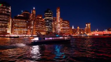 New York, ABD, 9 Aralık 2025: Hızlı bir tekne gece karanlık nehir manzarasında hareket ediyor. Arka planda New York 'un göz kamaştırıcı silueti.