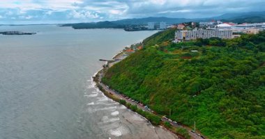 Köpüklü dalgalar yeşil tepelerle kıyıya ulaşır. Bulutlu bir günde Porto Riko şehrinde yükseliyor..