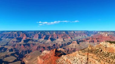 Parlak güneş ışığının aydınlattığı çarpıcı kaya oluşumlarının görüntüsü. Büyük Kanyon, Arizona, ABD üzerinde açık mavi gökyüzünde küçük beyaz bulut.