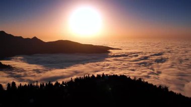 Dağlar arasında yoğun beyaz bulutların oluşturduğu muazzam bir manzara. Batan güneşin aydınlattığı kayanın yamacıyla dağılmış evlere bakın. Georgia mı? Hava görünümü.