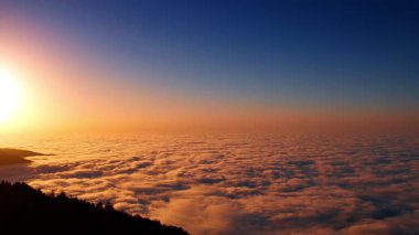 Batan güneş, dağlar arasındaki manzarayı kaplayan kalın bulutlu manzarayı renklendiriyor. Bulutlardan sarkan kayanın siyah silüeti. Hava görünümü.