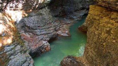 Su sarp duvarları olan kayalık bir kanyonda yavaşça hareket eder. Güneş ışığı suyun yüzeyine yansıyor. Sahne kayaların doğal güzelliğini ve dokusunu gösteriyor. Huzurlu bir nokta oluşturuyor..