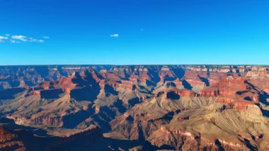 Parlak sabah güneşi, Arizona, ABD 'deki Büyük Kanyon manzarasını kamaştırır. Mavi gökyüzü, üzerinde küçük bulutlar.