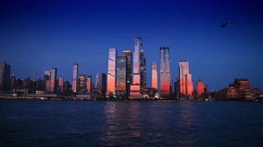 New York, ABD, 12 Aralık 2025: Helikopter gün batımında ABD 'nin New York kentine uçuyor. Batan güneş Manhattan 'ın ufuk çizgisindeki binaları aydınlatıyor..