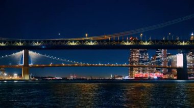 Brooklyn Köprüsü ve Manhattan Köprüsü gece aydınlatmayı açtı. Nehrin simgelerine alçak açıdan bak..