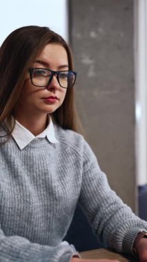 Modern geniş ofiste dizüstü bilgisayarda çalışan bir kadın. Klavyede yazan kadın aniden durur ve gözlüğüne dokunan şaşkınlığa bakar. Dikey video