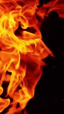 Alevler ve kıvılcımlar havaya ulaşıyor. Yanan şenlik ateşi siyah arka planda izole edilmiş. Dikey video