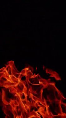 Alevlerin turuncu dilleri havaya yükseliyor. Siyah arka planda tehlikeli şenlik ateşi yanıyor. Dikey video