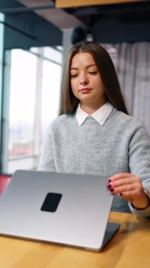 Gri kazaklı, uzun saçlı kadın bilgisayarını açıyor. Bilgisayarda serbest çalışan gülümseyen bayan. Arka plandaki adam masasına gelir ve çalışmaya başlar. Dikey video
