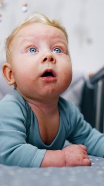 Sevimli sarışın çocuk karyolada huzur içinde yatıyor. Beşikteki göbeğin üzerinde duran güzel bir bebek portresi. Kapatın. Dikey video