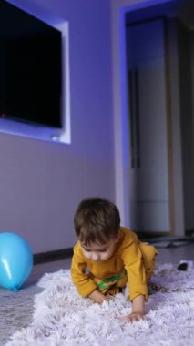 Küçük tatlı çocuk yere oturuverdi. Mutlu çocuk yumuşak yumuşak ekose üzerinde yuvarlanıyor. Dikey video