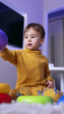 Piramitle oynayan tatlı sakin bir çocuk. Çocuk yerde oturup oyuncak monte ediyor. Düşük açı. Dikey video