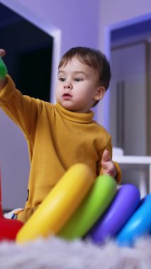 Oyuncak piramit toplayan sevimli odaklı çocuk. Sakin çocuk evdeki odasında oynuyor. Düşük açı. Dikey video