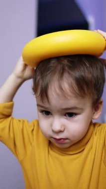Sarı kazaklı güzel esmer erkek çocuk oyuncaklarla oynuyor. Bebek oyuncak piramidin yüzüğünü kafasına yerleştiriyor ve bırakıyor. Kapatın. Dikey video