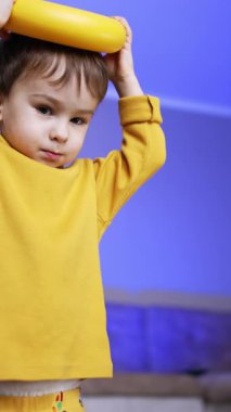 Siyah saçlı sevimli çocuk piramit halkasıyla oynuyor. Küçük çocuk oyuncağı kafasına koyuyor. Düşük açı. Kapatın. Dikey video