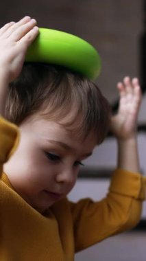 Güzel beyaz bir erkek bebek evde oynuyor. Küçük çocuk oyuncağı kafasına koyuyor. Kapatın. Dikey video