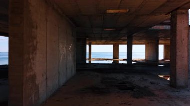Dış duvarları olmayan binanın zemininde hareket ediyorlar. Arkaplanda deniz manzarası.