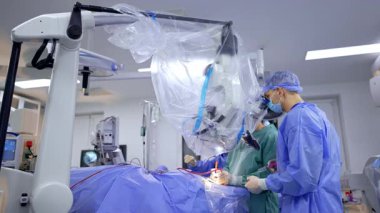 Çalışma yerinin üzerinde modern mikroskop var. Cerrahi ekip nörocerrahiyi elektrikli aletlerle gerçekleştiriyor..