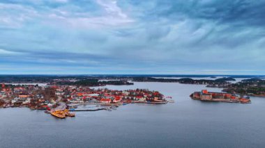 Malar Gölü üzerinde uçmak bulutlu gri gökyüzünü yansıtıyor. Stockholm takımadalarının başkenti Vaxholm 'ün parlak şehir manzarasına hava perspektifi.