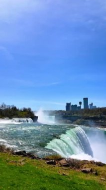 Amerika tarafından harika bir Niagara Şelalesi. Ontario vilayetinin siluetindeki binalar arka planda Kanada tarafında. Dikey video.