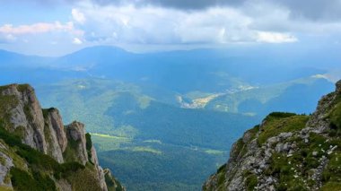 Yeşil vadilere ve uzak tepelere bakan bir dağ zirvesinden manzara. Yürüyüşçüler dağın tepesinden gökyüzünü çevreci tepeler ve aşağıdaki vadileri kaplayan bulutlara hayran..