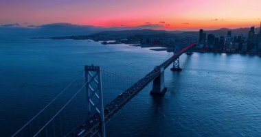 San Francisco-Oakland Bay Köprüsü yakınlarındaki su birikintisi üzerinde yoğun bir trafik var. Pembe gökyüzü gün batımından şehir manzarasının üzerine.