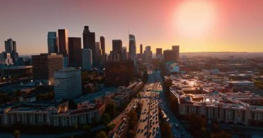 Şehirden yavaşça geçen birden fazla arabayla dolu çok şeritli otoyollar. İHA görüntüleri gün batımında Los Angeles, Kaliforniya 'nın yüksek binalarına yaklaşıyor..