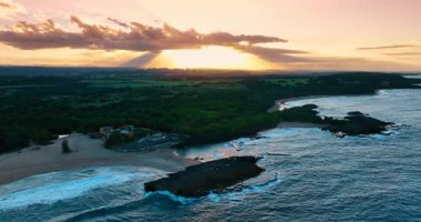 Şiddetli dalgalarla sahilin ötesindeki görüntüler. Bereketli yeşillik manzarayı kaplar. Bulutlar batan güneşi gökte gizler. Porto Riko.