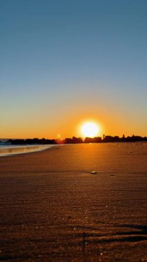 Okyanus dalgaları ve uzak kıyı şeridi ile kumlu sahilde gün doğumu. Güneş ufuktan yükselir, kumlu sahile ışık saçar..
