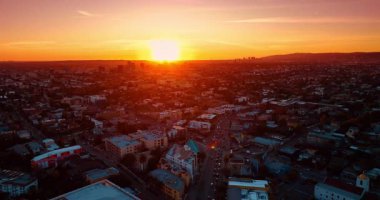 Batan güneşin parlak ışığı modern şehrin manzarasını kamaştırır. Otobanlarda İHA uçuşu, birden fazla araba hareket ediyor. Los Angeles, Kaliforniya, ABD.
