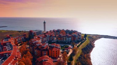 Sahne arkasında deniz feneri olan güzel Marina Cape Otel kompleksi. Bulgaristan 'ın Aheloy kentinde gün batımında Karadeniz kıyısında.