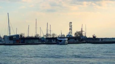 Burgaz, Bulgaristan, 29 Ekim 2025: Tekneler kıyı şeridi yakınlarında öğleden sonra limana yanaştı. Güneş su boyunca binaların arkasında batarken tekneler limanda park halindedir..