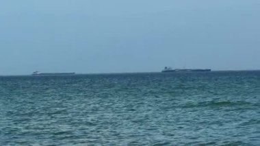 Gündüz vakti gemiler ufukta süzülüyor. Ufukta iki kargo gemisi görülüyor açık bir gökyüzünün altında mavi okyanus suyunun üzerinde.