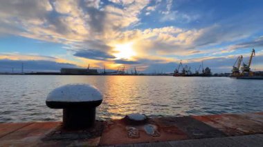 Limanda gün batımında, gökte bulutlar ve gemilerle birlikte. Güneş gemilerle ve bulutlarla dolu bir limanın üzerinde batıyor..