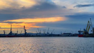 Burgaz, Bulgaristan, 29 Ekim 2025: Limanın üzerinde günbatımı uzaktaki vinçler ve gemilerle. Vinçler ve gemiler arka planda güneş batarken limanda görülür.