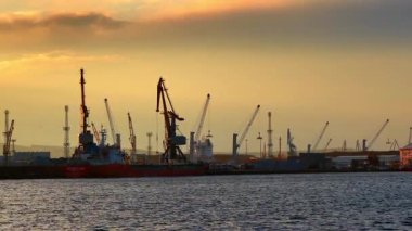 Burgaz, Bulgaristan, 29 Ekim 2025: Günbatımında arka planda vinçler ve kargo gemileriyle liman sahnesi. Gemiler bir limanda demirlerken, vinçler gün batımına karşı gölgede duruyor..