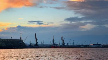 Burgaz, Bulgaristan, 29 Ekim 2025: Limanın üzerinde gün batımı ve suda vincler ve gemiler. Gün batımında kıyı şeridi boyunca gemi ve vinçlerle limanın görüntüsü.