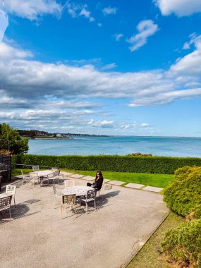 Açık havada verandada oturan bir kadın. Bir kadın açık havada verandada otururken deniz manzarasından zevk alır..