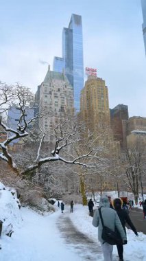 New York, ABD, 24 Aralık 2025: Yollar yayalar için kardan temizlendi. Central Park 'ta kar, New York, ABD. Şehir merkezindeki gökdelenler. Dikey video.