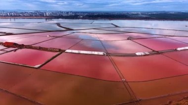 Tuz buharlaşma havuzlarında pembe ve turuncu su. Rıhtımda uçan İHA şehrin siluetine yaklaşıyor..