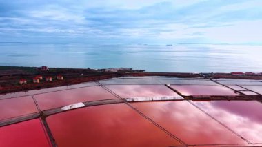 Gün batımında pembe tuz çiftliklerinin üzerinden uçacağız. Sonsuz mavi su manzarası ve arka planda bulutlu gökyüzü.