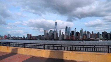 Doğu Nehri rıhtımındaki çitlere yaklaşıyoruz. Bulutlu bir günde New Jersey tarafından Manhattan 'ın muhteşem siluetini izlemek.