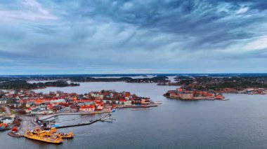 Deniz kenarında tekneli bulutlu bir günde kıyı kasabası manzarası. Kıyı kasabası, bulutlu gökyüzünün altında kıyıya yanaşmış teknelerle ve sahil boyunca uzanan binalarla deniz kıyısında yer alır..