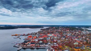 Bulutlu havalarda, tekneleri ve binaları olan kıyı kasabası manzarası. Kıyı kasabası deniz kenarında, limanda bulutlu gökyüzünün altında bir sürü tekne var..